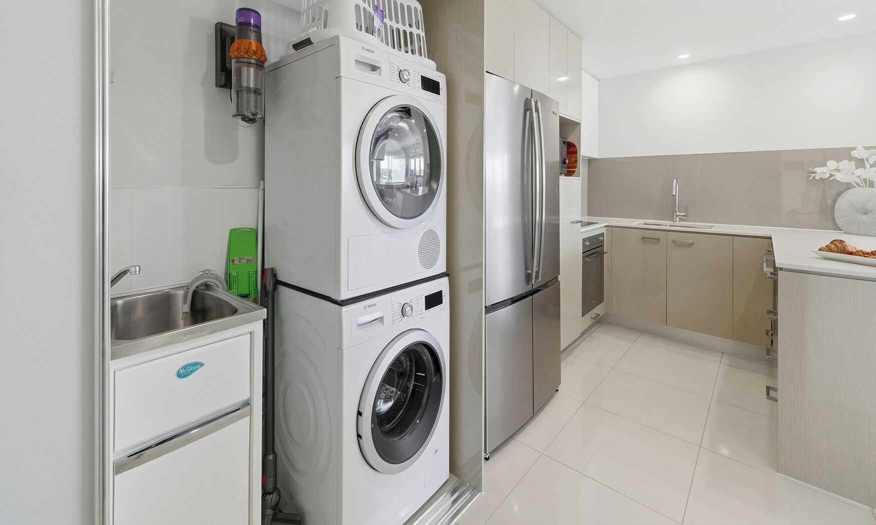 A modern kitchen with a Bosch washing machine, a stainless steel refrigerator, and a sink.
