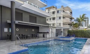A modern building with a pool, outdoor seating, and a balcony.