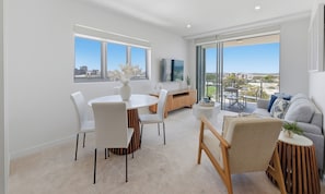 A modern living room with a dining area, large windows, and a view of the city. - Verve on Sixth (Maroochydore)