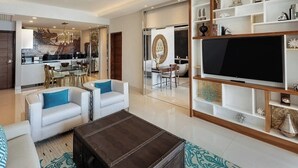A modern living room with a TV, white sofas, a coffee table, and a kitchen in the background. - Luxurious All-inclusive 2BR Suite at Garza Blanca Cancun  Thanksgiving Week 2026 (Cancún)