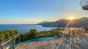 Um deck de madeira com guarda-corpo de vidro, com vista para um corpo d'água e uma paisagem montanhosa.