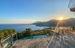 Eine Holzterrasse mit Glasgeländer, die auf ein Gewässer und eine Berglandschaft blickt.