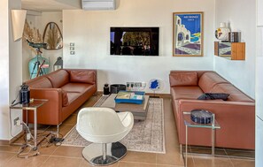 Ein Wohnzimmer mit zwei Ledersofas, einem weißen Sessel, einem Couchtisch, einem Fernseher und einem Gemälde.