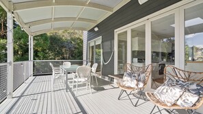 Eine überdachte Terrasse mit Tisch und Stühlen, einer Hängematte und Blick ins grüne Umland.