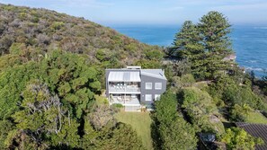 Ein zweistöckiges Haus mit Balkon, umgeben von üppiger Vegetation und mit Blick auf ein Gewässer.