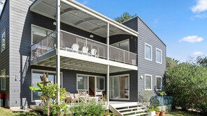 Ein zweistöckiges Haus mit Balkon, großen Fenstern und Außenbestuhlung.