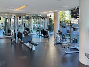 Ein modernes Fitnessstudio mit unterschiedlichen Trainingsgeräten, großen Fenstern und einer Sitzbank.