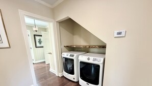 A laundry room with two front-loading washers and dryers, wooden flooring, and a white door leading to another room. - Wren House by Kirk Murphy Hospitality (Moultrie)