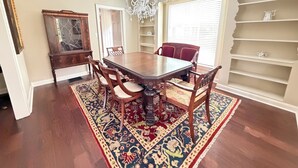 A dining room with a wooden table, chairs, a chandelier, a patterned rug, and a bookshelf. - Wren House by Kirk Murphy Hospitality (Moultrie)