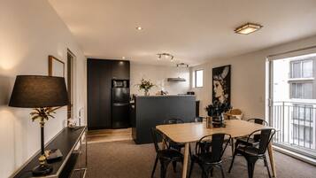 A modern kitchen with a central island, dining table with chairs, and a large window with a balcony.