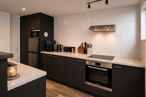 A modern kitchen with dark cabinetry, a stainless steel refrigerator, a microwave, a coffee maker, and a toaster.