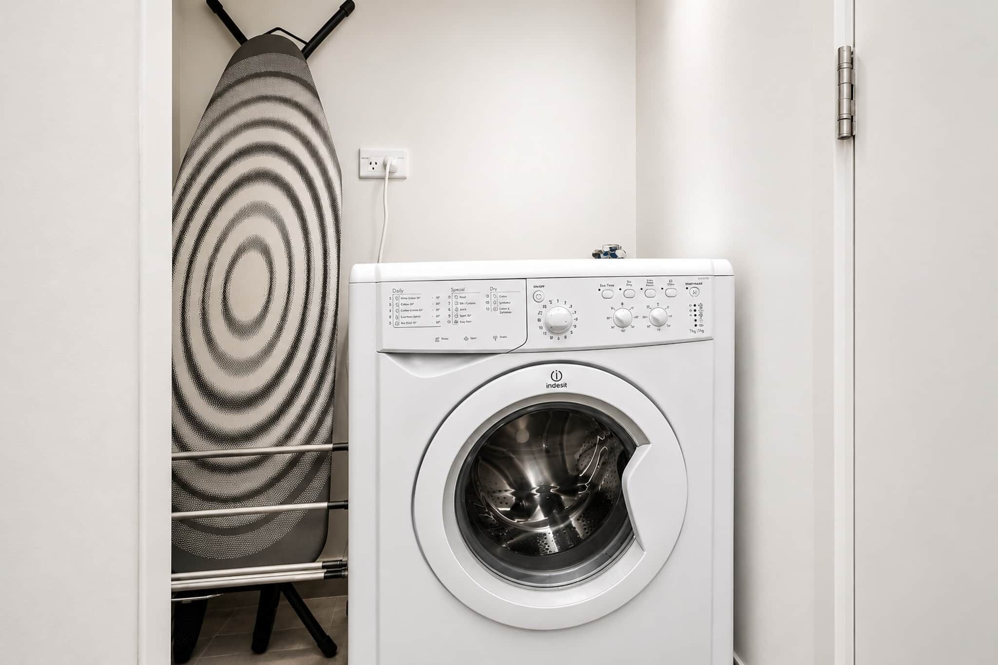 A front-loading washing machine with a control panel, a hanging drying rack, and a power outlet.