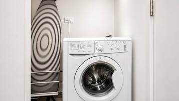 A front-loading washing machine with a control panel, a hanging drying rack, and a power outlet.