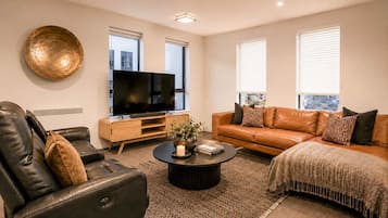A modern living room with a leather sofa, a coffee table, a flat-screen TV, and a large decorative plate on the wall.