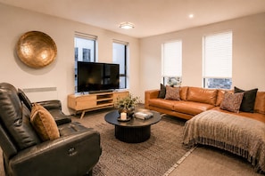 Ein modernes Wohnzimmer mit Ledersofa, Couchtisch, Flachbildfernseher und einer großen Wandplatte.