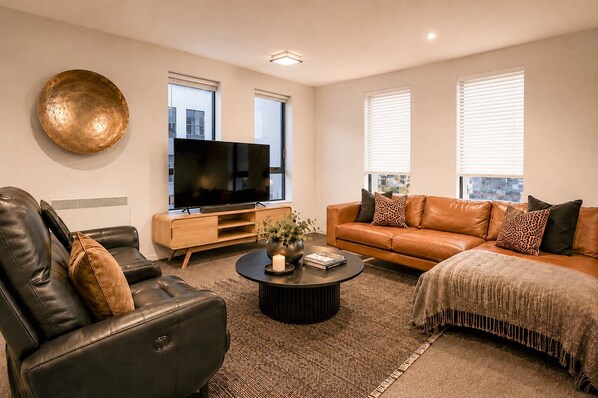 A modern living room with a leather sofa, a coffee table, a flat-screen TV, and a large decorative plate on the wall.