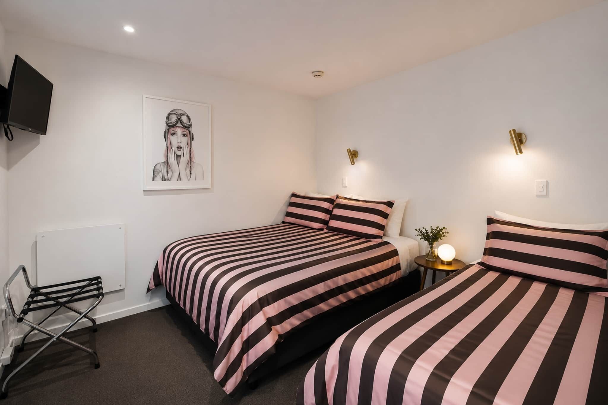 A bedroom with two beds, a radiator, a TV, and a wall-mounted light fixture.