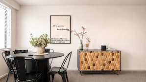 A dining area with a round table, black chairs, a wooden cabinet, and a framed quote on the wall. - Central CBD | Walk to Te Pae, Stadium + Parking (Christchurch)