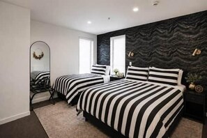 A bedroom with two beds, a mirror, a dresser, and a dark patterned wall. - Central CBD | Walk to Te Pae, Stadium + Parking (Christchurch)