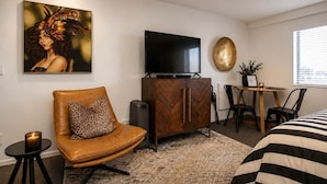 Ein Hotelzimmer mit Sofa, Fernseher, Schrank, Esstisch und einem Gemälde an der Wand.