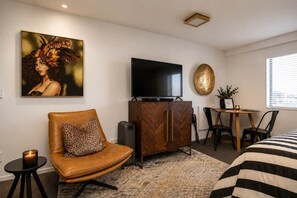 Een hotelkamer met een bank, een televisie, een kast, een eettafel en een schilderij aan de muur.