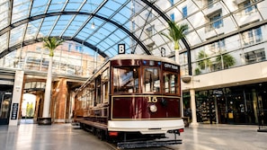 Een oude tram met de tekst 'CITY TOUR' en nummer 15, geparkeerd in een modern gebouw met een glazen dak en palmbomen.