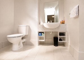A modern bathroom with a toilet, sink, and mirror. - Central Apt | Walk Te Pae + Parking (Christchurch)
