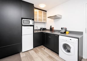 Eine kleine Küche mit Mikrowelle, Spüle und Waschmaschine, ausgestattet mit dunklen Schränken und heller Arbeitsplatte.