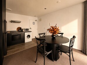 A compact living space with a dining area, kitchenette, and a washing machine. - Central Apt | Walk Te Pae + Parking (Christchurch)