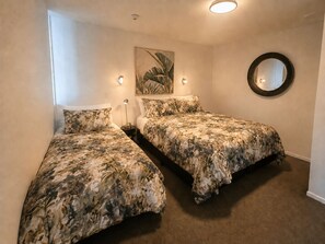 A bedroom with two single beds, a round mirror, and a wall-mounted light fixture. - Central Apt | Walk Te Pae + Parking (Christchurch)