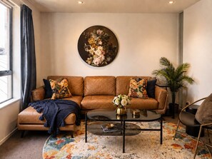 A living room with a brown leather sofa, a round coffee table, and a floral rug. - Central Apt | Walk Te Pae + Parking (Christchurch)
