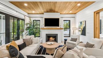 A modern living room with a fireplace, comfortable seating, and a large TV mounted above it.