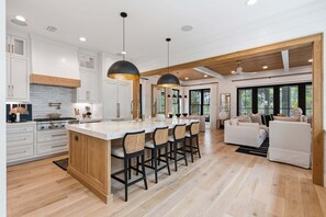 A modern kitchen with a central island, bar stools, and a dining area with a sofa and chairs. - NEW! WaterColor Phase 1 Location! LSV/Golf Cart & 4 Bikes Included! (Santa Rosa Beach)