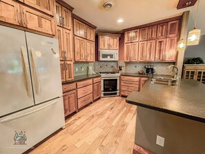 A kitchen with wooden cabinets, a refrigerator, a microwave, a stove, and a sink.