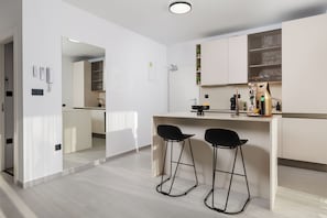 Eine moderne Küche mit Barbereich, zwei schwarzen Barhocker und einer Arbeitsplatte mit diversen Gegenständen.