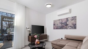 Ein modernes Wohnzimmer mit einer Couch, einem Fernseher, einem Couchtisch mit Kerzen und einem großen Fenster.