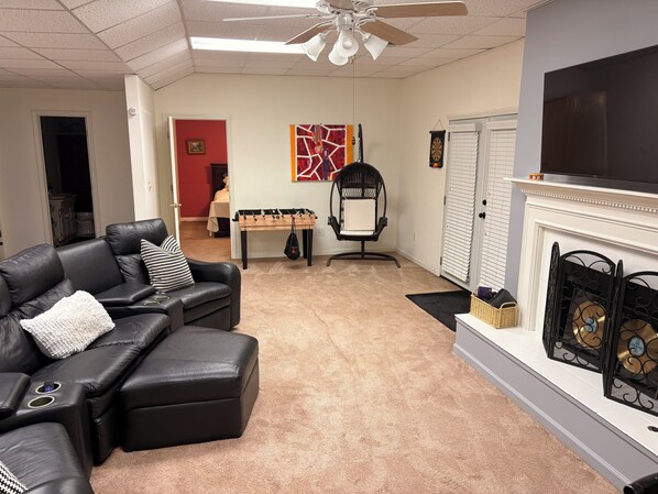 A living room with a leather sofa, a foosball table, a black chair, and a fireplace.
