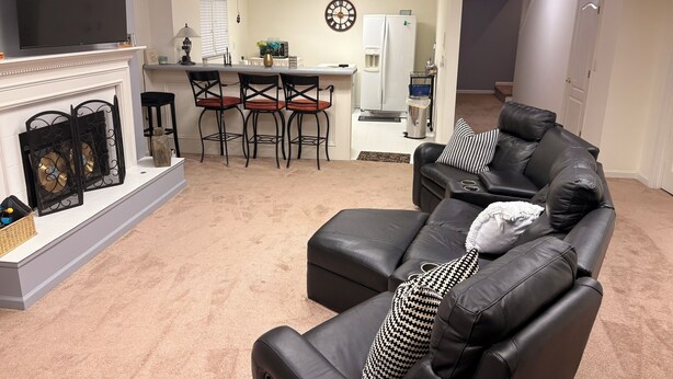 A living room with a fireplace, a television, a sofa, and a kitchen area in the background. - Welcoming 2-bedroom basement apartment with AC in vibrant Atlanta (Atlanta)