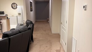 A hallway with a beige carpet, a black leather couch, a clock on the wall, and a white door at the end. - Welcoming 2-bedroom basement apartment with AC in vibrant Atlanta (Atlanta)