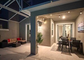 An open-plan living area with a sofa, dining table, and chairs, a potted plant, and string lights. - Luxury Disney Retreat: Pvt Pool + Resort Access (Kissimmee)