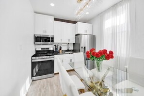 Una cocina moderna con armarios blancos, electrodomésticos de acero inoxidable y una mesa de comedor de vidrio con un florero de rosas rojas.
