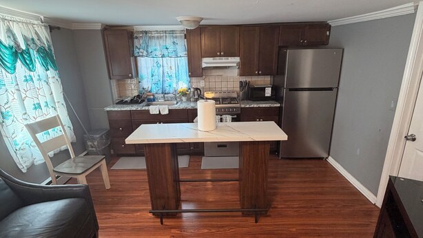 A kitchen with wooden cabinets, a stainless steel refrigerator, a dining table, and a sofa. - Elite room stay (Bridgeport)