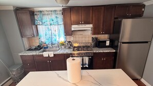 A kitchen with wooden cabinets, a marble countertop, a gas stove, a microwave, and a stainless steel refrigerator. - Elite room stay (Bridgeport)