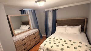 A bedroom with a wooden bed, a dresser, a mirror, and a ceiling light. - Elite room stay (Bridgeport)