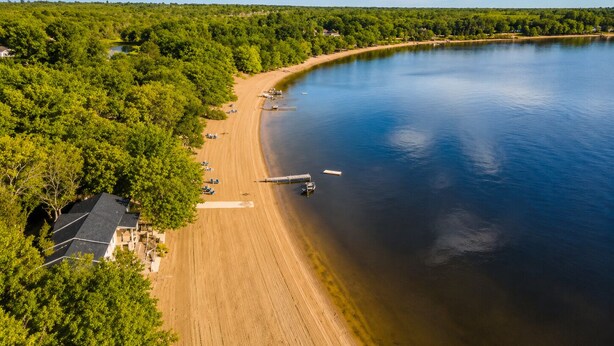 An aerial view of a lakeside property with a sandy beach, dock, and surrounding forest. - Cozy Beach Escape/Fire pit/Sunrises/Lake Views/Golf/Pickleball/45 to Fredericton (Canning)