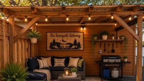 A cozy outdoor seating area with a wooden pergola, a sign reading 'The Sunnyside Getaway,' and a grill station. - Cozy Beach Escape/Fire pit/Sunrises/Lake Views/Golf/Pickleball/45 to Fredericton (Canning)