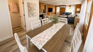 A compact living space with a dining area, kitchen, and seating area. - Cozy Beach Escape/Fire pit/Sunrises/Lake Views/Golf/Pickleball/45 to Fredericton (Canning)