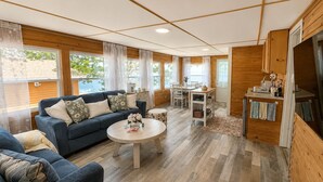 A cozy living room with a sofa, a coffee table, and a dining area with a table and chairs. - Cozy Beach Escape/Fire pit/Sunrises/Lake Views/Golf/Pickleball/45 to Fredericton (Canning)