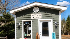 A small building labeled 'Kellar Crafts' with a white door, a bench with a sign, and a welcome sign.