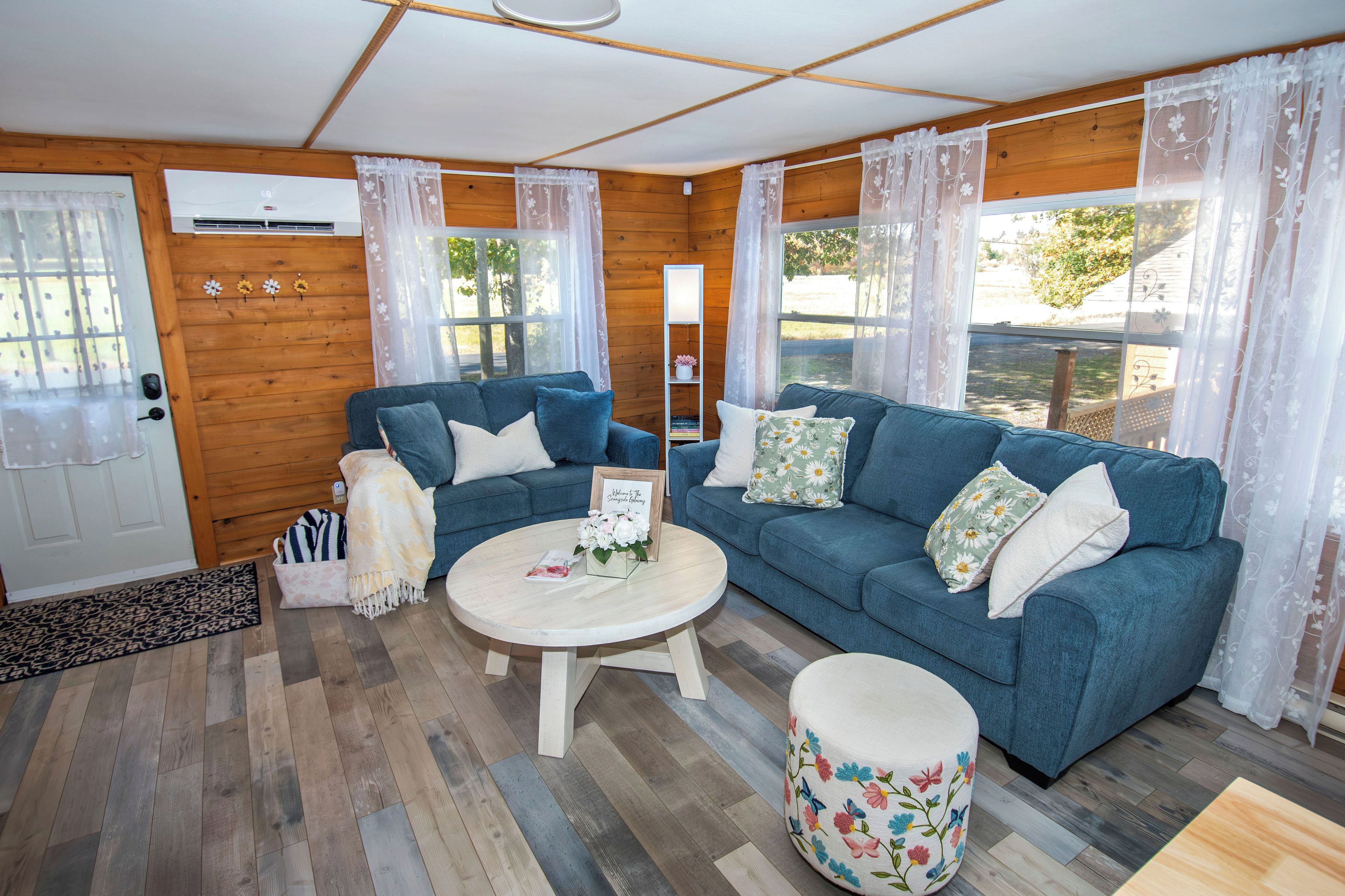 A cozy living room with a blue sofa, a round coffee table, and a floral ottoman.